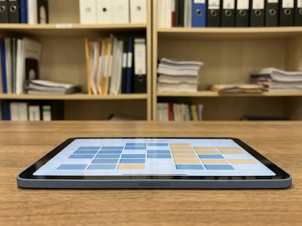Tablet met kleurgecodeerd digitaal rooster op bureauoppervlak, met hotelkantoor op de achtergrond.